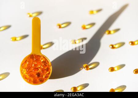 Capsule di gel trasparente gialle di vitamina d o omega 3 in cucchiaio su fondo grigio alla luce solare. Foto Stock