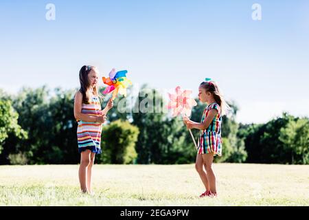 Due bambine che soffiano su pinwheels colorati nel parco. Amici che giocano all'aperto. Foto Stock