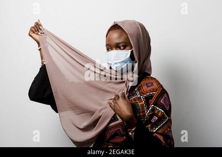 Donna d'affari musulmana nera in maschera medica strizzata in hijab su sfondo bianco. Investimenti di criptovaluta in bitcoin. Ragazza nera riuscita. Foto Stock