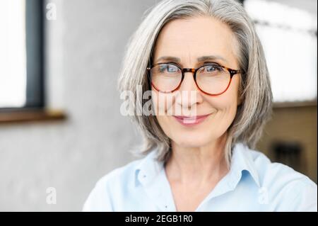 Primo piano ritratto di affascinante positiva anziana donna di affari che indossa occhiali eleganti e abbigliamento casual elegante. Senior fiducioso con capelli grigi Foto Stock