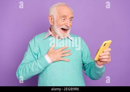 Ritratto fotografico dell'uomo anziano che legge notizie sulla mano dello smartphone sul petto sovrascherzato isolato su sfondo di colore viola pastello Foto Stock