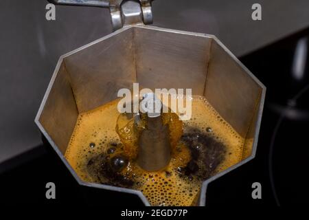 Il caffè liquido esce da una caffettiera che si trova sulla stufa in cucina. Caffè con la sua crema all'interno di una macchina da caffè italiana tipo 'Moka' Foto Stock