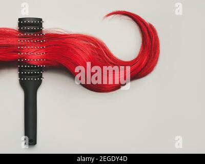 spazzola per capelli con ciocca di capelli rossi femminili su un grigio Background.Hairdresser salone e concetto di acconciature Foto Stock
