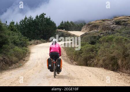 Ciclista femminile in bicicletta pesante carico con grandi panniere su strada sterrata attraverso le Ande, Vallegrande Provincia, Santa Cruz, Bolivia Foto Stock
