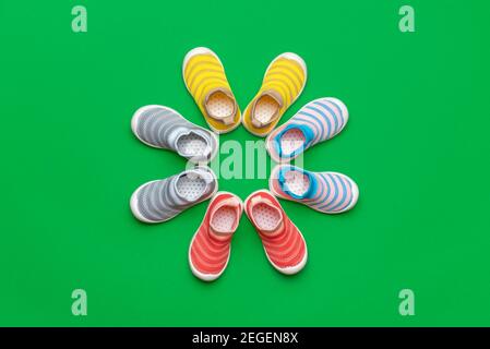 Posa piatta con quattro paia di scarpe per bambini multicolore isolate su uno sfondo di colore verde. Scarpe colorate disposte a cerchio. Foto Stock