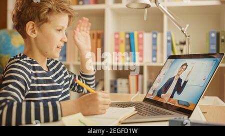 Smart Little Boy utilizza il laptop per videochiamare con il suo insegnante. La schermata mostra la lezione online con l'insegnante dà il benvenuto allo studente con il gesto ondulato, Boy Foto Stock