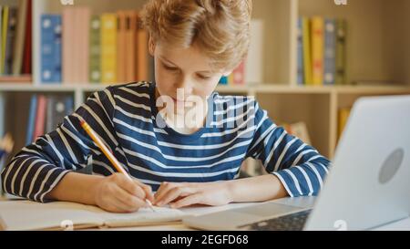 Smart Little Boy utilizza il laptop per l'apprendimento, scrive informazioni utili. Apprendimento a distanza, e-Education, e-Learning, concetto di Homeschooling. Verticale Foto Stock