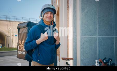 Happy Food Delivery uomo che indossa lo zaino termico in bicicletta consegna l'ordine del ristorante. Sorridente Courier guardando la fotocamera. Il corriere consegna il pranzo al takeaway Foto Stock