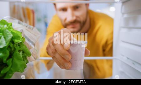 Camera interna cucina Frigo: Bell'uomo apre Frigo porta, take out yogurt. Uomo che mangia sano. Punto di vista POV Shot da frigorifero pieno di Foto Stock