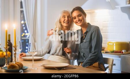 Multi generazioni di belle donne in cucina. Madre anziana e figlia matura siedono a un tavolo e abbraccio, divertirsi e sorridere sulla fotocamera. Bella famiglia Foto Stock