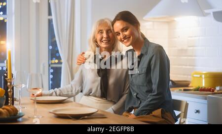 Multi generazioni di belle donne in cucina. Madre anziana e figlia matura siedono a un tavolo e abbraccio, divertirsi e sorridere sulla fotocamera. Bella famiglia Foto Stock