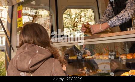 Giovane donna che acquista un pranzo da un chiosco gourmet all'aperto che offre panini, pane, caffè da asporto e cibo da asporto nella pausa pranzo. Misura di sicurezza Foto Stock