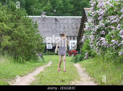 Piccola ragazza felice in abito a righe cammina sulla casa edificio sullo sfondo in campagna Foto Stock