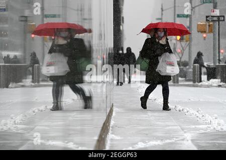 New York, Stati Uniti. 18 Feb 2021. La vista divisa di una donna e la sua riflessione come lei tiene un ombrello rosso mentre cammina lungo la 6th Avenue nel centro di Manhattan durante una tempesta invernale prevista per portare più di un piede di neve nei prossimi due giorni, New York, NY, 18 febbraio 2021. Il Servizio meteorologico Nazionale ha emesso un orologio invernale per la zona tri-state, come gran parte della nazione soffre attraverso l'esplosione invernale negli ultimi giorni. (Foto di Anthony Behar/Sipa USA) Credit: Sipa USA/Alamy Live News Foto Stock