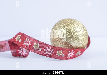 Una palla dorata scintillante con nastro di Natale rosso sul sfondo bianco Foto Stock