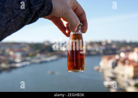 Piccola bottiglia di vino di porto all'aperto con Il fiume Douro e la città di Porto sullo sfondo blu Foto Stock