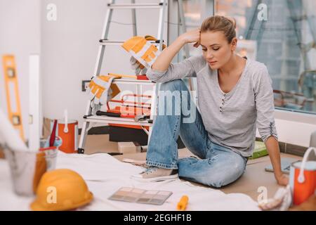 Pretty Woman siede in una stanza preparata per la ristrutturazione e seleziona un colore per una pittura di parete. Design interno del nuovo appartamento. Foto Stock