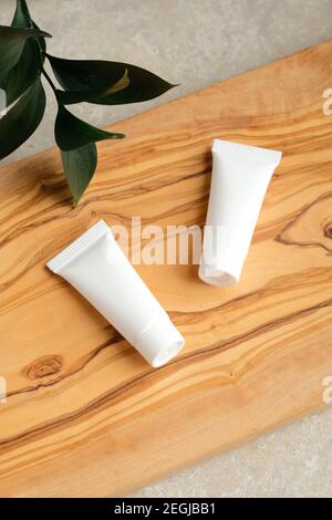 Confezione di tubi con lozione cosmetica e foglia verde su tavola di legno. Bianco vuoto cosmetici contenitori crema design, branding Foto Stock