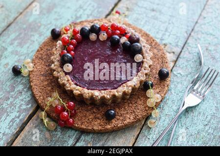 Piccole crostate vegane a base di noci e confettura di bacche decorate con ribes nero, rosso e bianco sul guardaroba di sughero Foto Stock