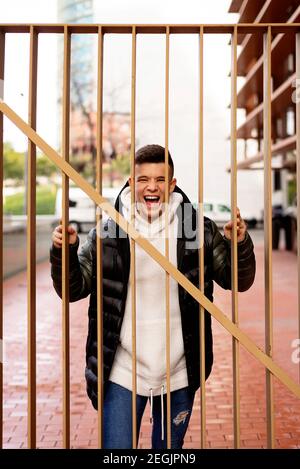 Giovane ragazzo in piedi dietro una recinzione di metallo mentre guarda la macchina fotografica Foto Stock