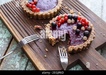 Piccole crostate vegane a base di noci e confettura di bacche decorate con ribes nero, rosso e bianco su chiocciola in legno di quercia Foto Stock