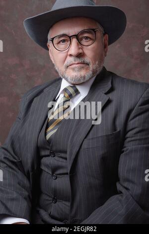 Un Signore maturo che posa per la macchina fotografica in un buio tuta e cappello marrone Foto Stock