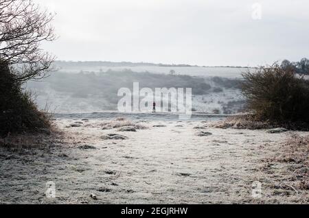 Donna che cammina lungo un sentiero ghiacciato nella campagna inglese in inverno Foto Stock