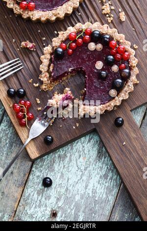 Dolci vegani. Torta aperta fatta di mandorle e gelatina di frutti di bosco decorata con ribes nero, rosso e bianco crudo su tavola di quercia copyspace sopra la vista Foto Stock