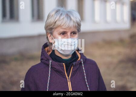 Ritratto di una donna penosa e triste di mezza età in piedi per strada indossando una maschera respiratoria per proteggere la sua salute. Primo piano. Concetto di protezione. Foto Stock