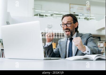 L'uomo d'affari maturo riuscito overjoyed ha ottenuto una promozione di lavoro o ben fatto con il progetto importante. Eccitato imprenditore caucasico ricevere grande profitto o ha ottenuto un buon affare Foto Stock