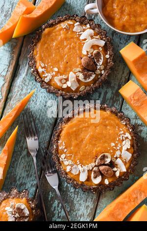 Dolce vegano sano. Crostate fatte in casa con noci e farina d'avena e ripieno di zucca servita con zucca cruda su sfondo blu sopra la vista Foto Stock