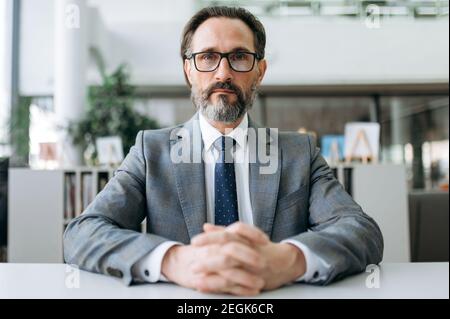 Webcam ritratto di leader maschile intelligente in abito e occhiali di stile. Uomo d'affari maturo di successo guarda direttamente alla telecamera Foto Stock