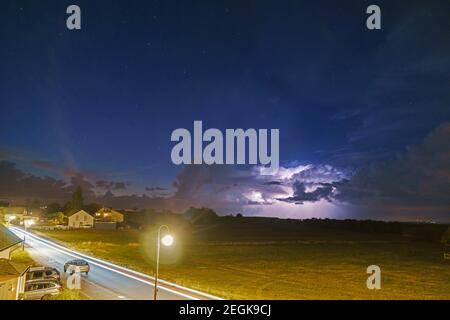 Lampi in nuvole tempesta su prato in tedesco villaggio oltre una strada di notte Foto Stock