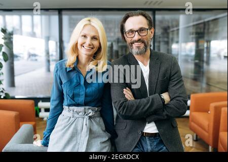 Ritratto di eleganti colleghi di mezza età in ufficio. Le persone che lavorano con successo sono sicure di stare in un ufficio moderno, guardando e sorridendo la fotocamera Foto Stock