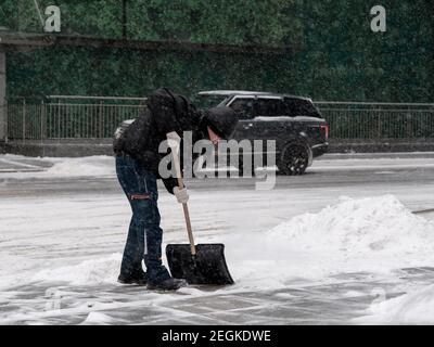 Mosca. Russia. 12 febbraio 2021. Un operatore di servizi che indossa una maschera protettiva, indossa una pala per la neve su una strada cittadina durante una nevicata su un Foto Stock