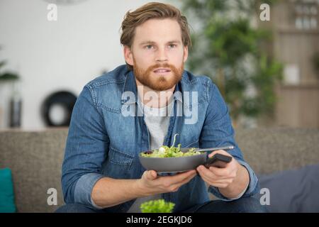 uomo che mangia un'insalata mentre guarda la tv Foto Stock