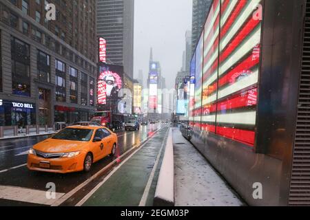 18 febbraio 2021 : UNA tempesta di neve leggera ha colpito New York City. Un taxi passa davanti alla bandiera degli Stati Uniti illuminata a Times Square Foto Stock