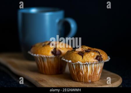 Muffin al cioccolato appena sfornati e una tazza di caffè su un piatto di legno con fondo nero Foto Stock