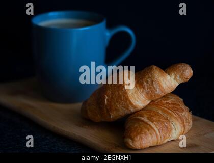 Una tazza di caffè e croissant per la colazione con un sfondo nero Foto Stock
