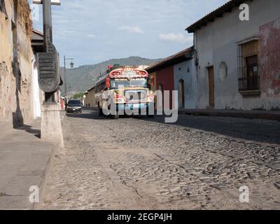 Guatemala, Antigua - 26 maggio 2019 - Chicken bus su una strada di ciottoli in Antigua guatemala, case stagioate, catena montuosa sullo sfondo Foto Stock