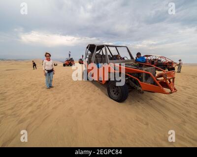 Perù, Ica - 21 settembre 2019 - Donna posa accanto al buggy al deserto, alcuni turisti si trovano sul tetto del buggy Foto Stock