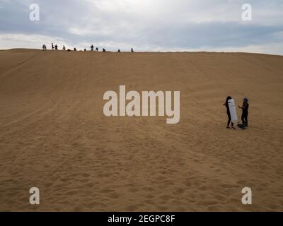 Perù, Ica - 21 settembre 2019 - sandboarding turistico nel deserto di Ica in Perù, alcuni turisti si preparano e due donne in piedi lungo la duna di sabbia Foto Stock