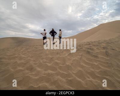 Perù, Ica - 21 settembre 2019 - i turisti degli alberi godono della vista del deserto che si erge sulla cima di una duna sotto il cielo blu Foto Stock