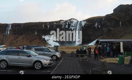 Islanda, Seljalandsfoss - 2 dicembre 2017 - cascata visto dal parcheggio, i turisti acquistano souvenir alla piccola capanna Foto Stock