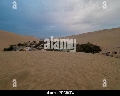 Vista completa dell'oasi di Huacachina nel deserto di Ica in Perù, sabbia in primo piano e dune sullo sfondo Foto Stock