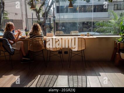 Peru, Lima - 28 settembre 2019 - due donne mangiano di fronte alla finestra che domina gli edifici sulla strada Foto Stock