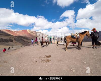 Perù, Vinicunca - 1 ottobre 2019 - turisti e cavalli in cima a una montagna sotto il cielo blu Foto Stock
