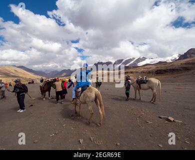 Perù, Vinicunca - 1 ottobre 2019 - cavalli, turisti e locali sulle montagne delle Ande in Perù, neve montagna in lontananza Foto Stock