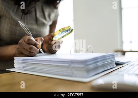 Indagine sulle frodi aziendali. Auditor che usa la lente di ingrandimento per indagare Foto Stock