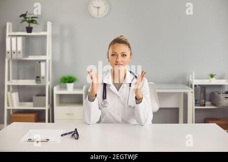 Giovane positivo biondo femmina medico infermiera terapeuta seduta, parlando online con paziente Foto Stock
